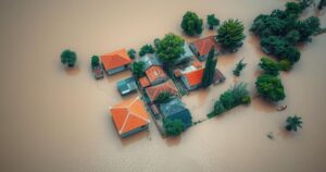 Aerial view of submerged market town with brown floodwaters covering buildings and landscape, highlighting climate impact.