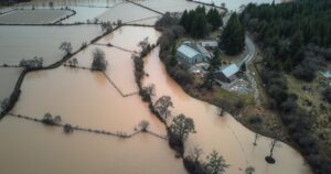 Aerial view of a flooded rural landscape with submerged fields, trees, and debris, showing the impact of severe weather.